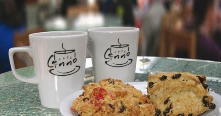 Two white Café Cenno mugs and two fruit scones on white plate.