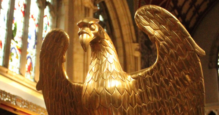 Close-up of gold eagle lectern. Stained glass window in background.