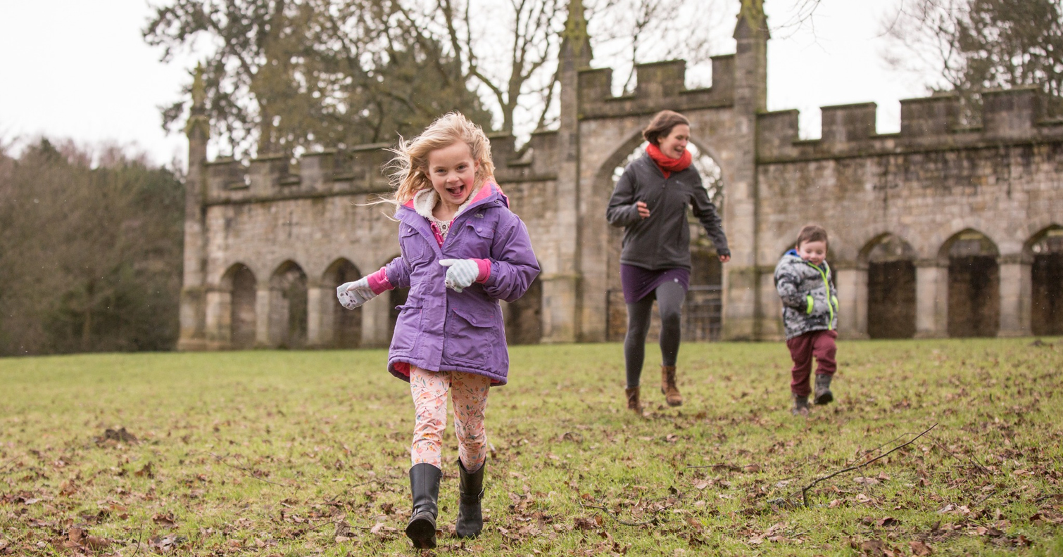 woman and two children running through deer park at Auckland Castle with deer house in background