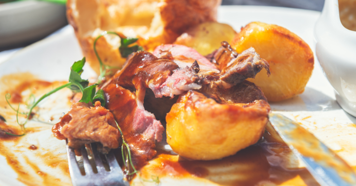 Sunday Roast showing knife and fork on plate with meat, gravy roast potatoes Yorkshire Pudding and garnish.