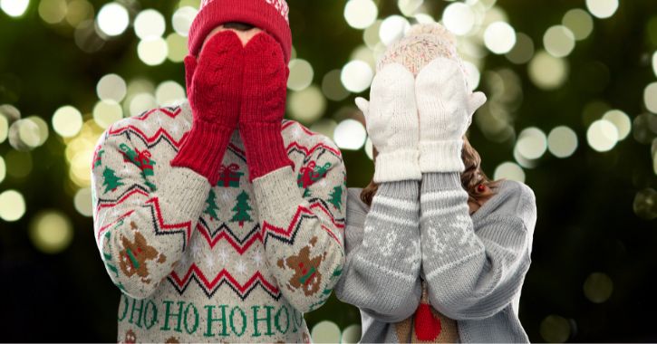 man and woman wearing christmas jumper and mittens covering their faces against a festive sparkle background