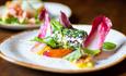 A speckled dinner plate with a dark coloured rim. A brightly coloured serving of food with red salad leaves to decorate.