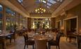 Tables set up in a restaurant at dusk. Candles are lit on tables and chandelier light is switched on.