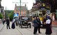 The 1900s Town Street at Beamish Museum filled with costumed engagers, cars, buses, motorbikes and a tram