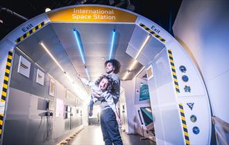 A man and a child playing in a replica of the International Space Station at the Life Science Centre.